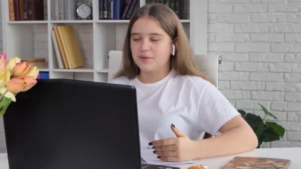 若い女性は 自宅で働く オンライン教師の勉強とノートパソコンの話を呼び出すヘッドセット会議を身に着けています コンピュータのウェブカメラのチャットを使用して学ぶ女性学生はノートを作る 距離教育 — ストック動画