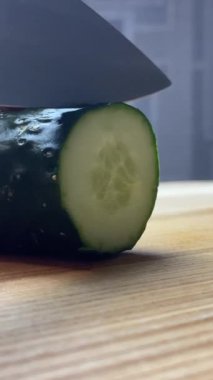 Dikey ekran: Mutfak bıçağı ve ahşap tahta kullanarak yeşil salatalıkları dilimleyen genç bayan ev kadınlarının aşırı yakın çekimi. Salata hazırlanıyor.