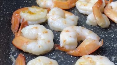 Kızartma tavasında kızartılmış karides. Yakın plan. Gaz ocağında tavada büyük karides pişirmek. Aşçı kızartma tavasında spatula kullanarak karidesi zeytinyağına karıştırıyor. Deniz ürünleri pişiriyorum.