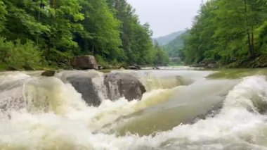 Dağ nehri su yüzeyi ağır çekimde. Dağ nehrinde dalgalar oluşturan temiz bir dere. Akan su arka planına yakın çekim. Taştan akıntılar arasında akan hızlı bir akış. Dağ nehrinin yakınında.