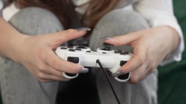 Tırnakları boyalı genç bir kız. Konsol oyunlarına dalmış bir genç. Koltukta joystick ile oyun sahnesi.