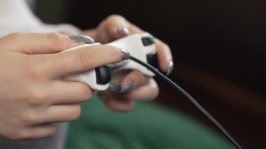 Tırnakları boyalı genç bir kız. Konsol oyunlarına dalmış bir genç. Koltukta joystick ile oyun sahnesi.