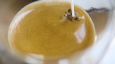 Adding coffee creamer into black coffee. Slow motion cream pouring in a cup of black coffee