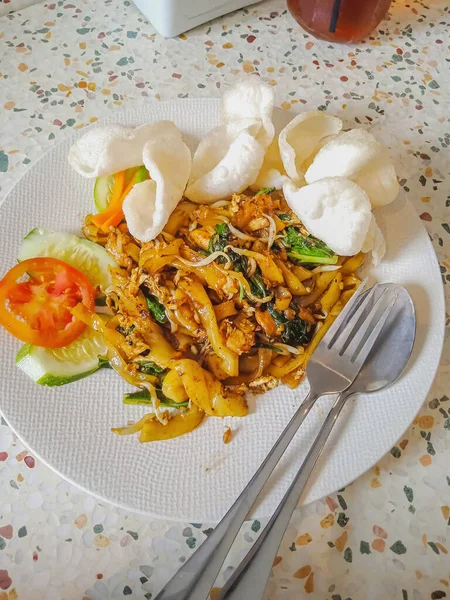 Kızarmış Kwetiau beyaz tabakta servis ediliyor. Kızarmış Kwetiau Endonezya 'da yaygın bir Çin yemeğidir..