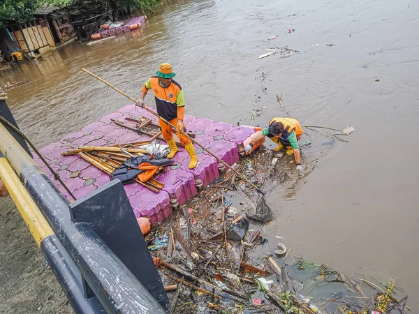 Jakarta, Endonezya - 24 Şubat 2023: İki temizlikçi köprünün altında sıkışan çöpü çözüyor. Jakarta bölgesinde yüksek yoğunluktaki yağmur Sungai Banjir Kanal Barat 'ın taşmasına neden oldu..