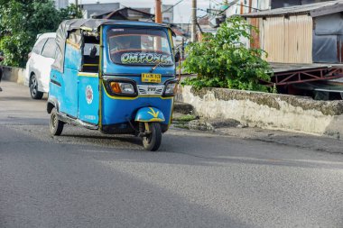 Jakarta, Endonezya - 1 Nisan 2023: Cakarta, Endonezya 'da üç tekerlekli bir taksi asfalt yolda ilerliyor.