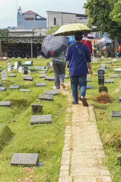 Cakarta, Endonezya - 14 Nisan 2024: Kurban Bayramı 'ndan sonra mezarlıkta yürüyen şemsiye kullanan insanların arka planı.