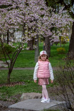 Güzel sarışın kız bahar bahçesinde yürüyor, pembe çiçekler, çiçek açan sakura