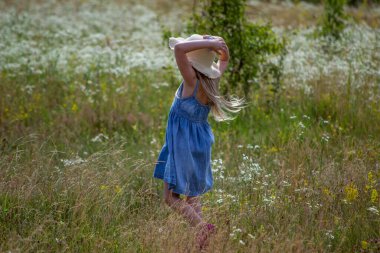 Yazın tarlada yürüyen beyaz şapkalı küçük kız.