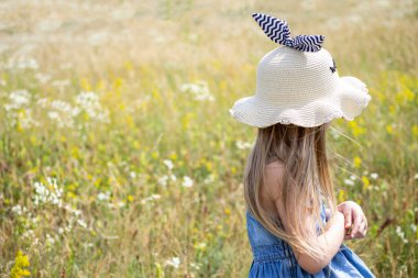 Yazın tarlada yürüyen beyaz şapkalı küçük kız.