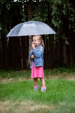 Çimlerde şemsiyesi ve çizmeleri olan küçük tatlı kız.