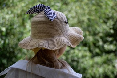 Yeşil yapraklı arka planda şapkalı ve atkılı bir kız.