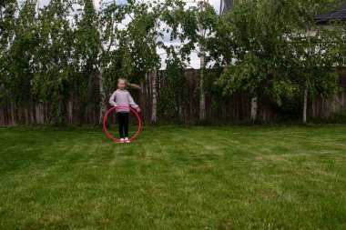 Genç bir kız yazın parkta çimenlikte hulahopla oynuyor.