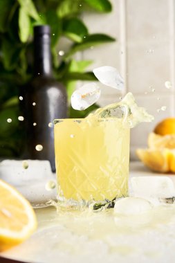 Geleneksel İtalyan ev yapımı limonata içeceğinin üzerine buz düşüyor. Mutfak tezgahında limon parçaları olan limoncello.