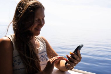 Feribot yolculuğu sırasında gülümseyen genç bir turistin telefonda konuşması..