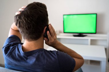 worried man talking on the phone while watching the news on the sofa. TV with chroma key