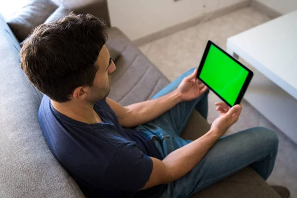 young man using a green screen tablet while working from home living room.