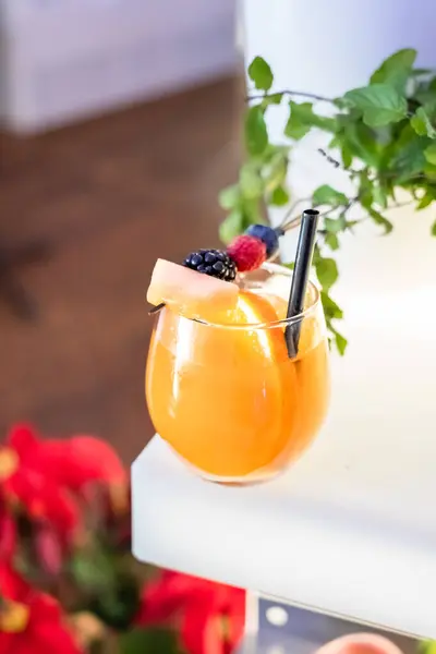 Barda kırmızı dutlarla süslenmiş bir bardak portakal kokteyli.