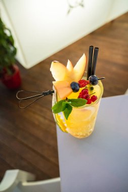 Barda kırmızı dutlarla süslenmiş bir bardak portakal kokteyli.