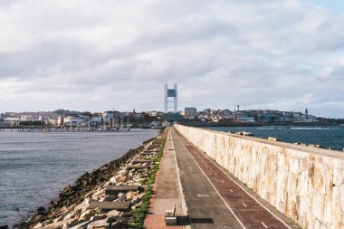 A Coruna, İspanya 'da manzaralı bir sahil yolu işaretli yolda tek bir mavi bisiklet var. Gezinti alanı arka plandaki şehre doğru uzanır, her iki tarafında deniz bulunur ve yeşil bir kemerle çerçevelenir. Seyahat için ideal, kentsel siklin