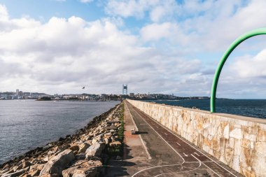 A Coruna, İspanya 'da manzaralı bir sahil yolu işaretli yolda tek bir mavi bisiklet var. Gezinti alanı arka plandaki şehre doğru uzanır, her iki tarafında deniz bulunur ve yeşil bir kemerle çerçevelenir. Seyahat için ideal, kentsel siklin
