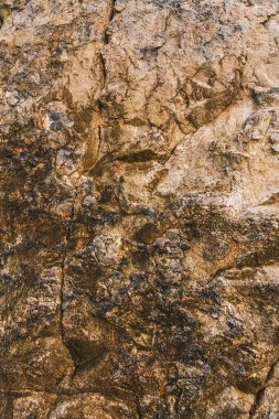 Engebeli bir kaya yüzeyinin karmaşık dokularını dünyevi tonlarla gösteren yakın plan bir görüntü. Bu doğal doku, taşın kaba ve çatlak görünümünü vurgulayan detaylar bakımından zengindir. Arkaplan, doku örtüsü veya jeol olarak kullanmak için ideal