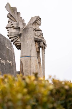 Bir melek savaşçının modern taş heykeli açısal detaylar ve bir kılıç ile. Gücü, dayanıklılığı ve tarihi simgeleyen çarpıcı bir anıt..