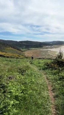 Sahilde ve ormanlık tepelerde koşan bir kadının arka görüntüsü.
