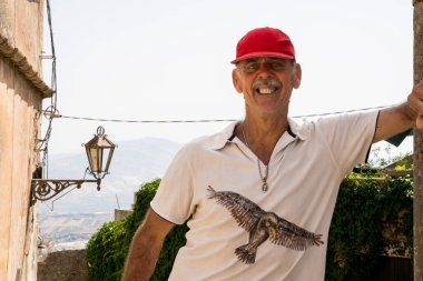 Avrupa 'nın tarihi bir şehrinin kaldırım taşı sokağında poz veren kırmızı şapkalı mutlu kıdemli adam. 