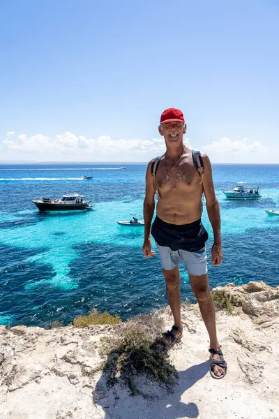 Sırt çantalı yaşlı adam yaz gününün tadını çıkarıyor. Favignana, İtalya 'da turkuaz deniz kenarında.