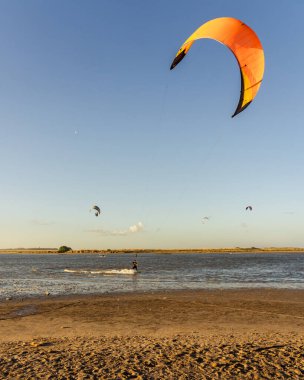 Doğayla ve sıcak ışıkla çevrili, gün batımında bir deniz gölünde uçurtma yüzen bir insan.