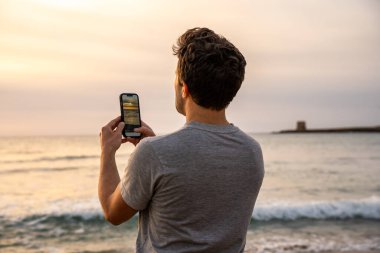 Kumsaldan gelen telefonuyla gün batımını yakalayan genç adam.