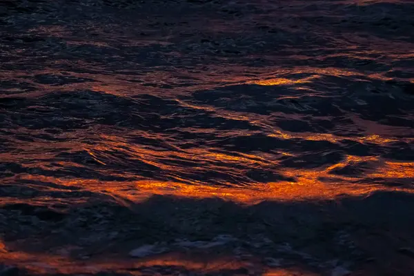 Dalgalar, kayalar ve kumsalda parlayan günbatımıyla dolu canlı bir deniz manzarası.