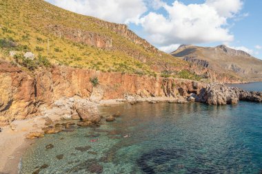 Sicilya 'da tenha bir kayalık koyda turkuaz suda yüzen iki kişi.