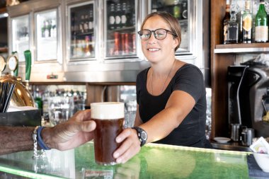 Barda müşteriye köpüklü bira servisi yapan dost canlısı bir bayan barmen.