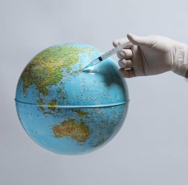 hand in protective medical mask holds globe with syringe. coronavirus covid - 19 pandemic concept.