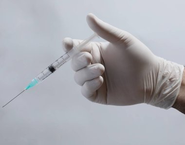 Siyah arka planda şırıngası olan tıbbi maskeli bir doktor..