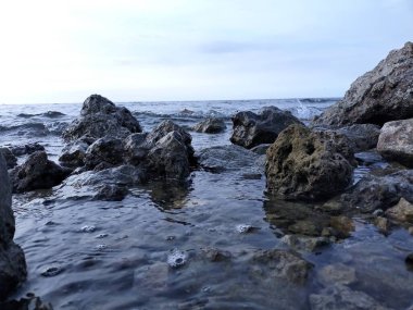 Küçük dalgalar mavi gökyüzü arka planıyla kayalara çarpıyor.