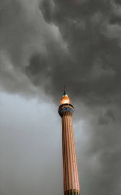 Güzel süslenmiş bir minare, kara ve çalkantılı bulutların ardından gururla yükselir. Karmaşık şablonlar ve en üstteki altın aydınlatma inancı ve dayanıklılığı simgeler. Fırtına yaklaşırken bile dimdik ayakta durur..