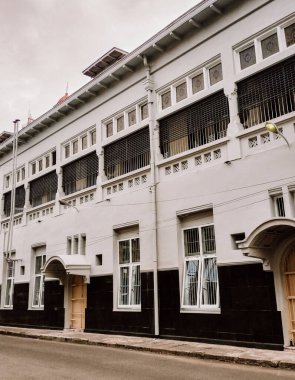 Kemerli camlar, dekoratif ızgaralar ve temiz krema ve siyah faade içeren klasik koloni tarzı bir binanın yakın plan görüntüsü. Binalar simetri ve detay tarihi cazibeyi yansıtıyor.