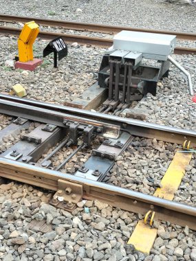 Bir mekanik demiryolu anahtarı, pist donanımı, manivelayı ve elektrik kontrol kutusunu gösteriyor. Görüntü, trenlerin rayları değiştirmesini sağlayan karmaşık mühendisliğe yakından bakmamızı sağlıyor. Çelik, engebeli bir endüstriyel ortam yaratıyor.
