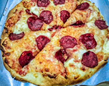 Bu fotoğrafta altın-kahverengi kabuklu ve erimiş peynirli nefis bir pepperoni pizza var. Pizza dilimleniyor, servis edilmeye hazır, ve zengin, lezzetli sosları onu görsel olarak iştah açıcı kılıyor..