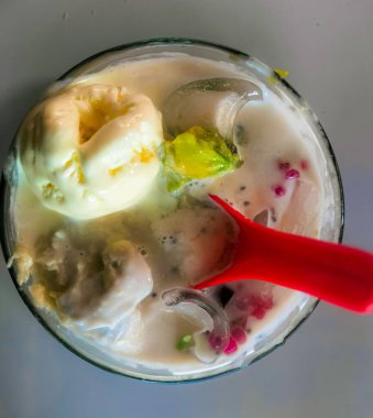 Bu canlı yakın çekim vitrinleri bardakta sunulan tropikal bir tatlı. Dondurma, tıraş edilmiş buz, jöle, avokado ve diğer renkli tatlı malzemeler karışımı içerir. Tazeleyici ve hoşgörülü bir görünüm verir. Tatlının içine kırmızı bir kaşık konur.