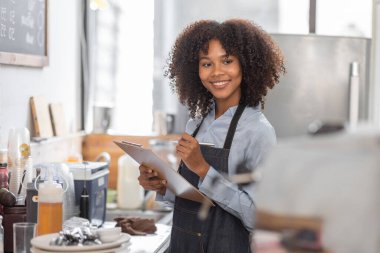 Afrikalı kadın kahve dükkanı küçük işletme sahibi tezgahın önünde durup stok kontrolü yapıyor. afro saç çalışanı Barista girişimci.