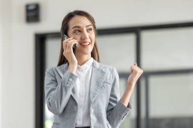 Gülümseyen mutlu iş kadını cep telefonuyla konuşuyor, iş yerinde elinde belgelerle duruyor.