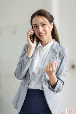 Gülümseyen mutlu iş kadını cep telefonuyla konuşuyor, iş yerinde elinde belgelerle duruyor.