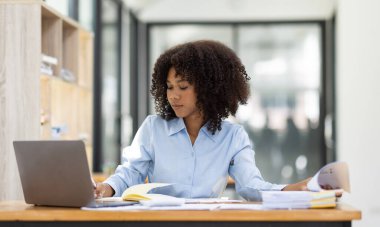 Başarılı Afro-Amerikan muhasebeci kadın ofisteki dizüstü bilgisayardan evrak vergisi alıyor. Yatırım ekonomisi ve pazarlama araştırma kavramını finanse et.