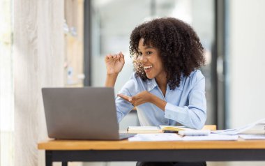 Güzel Asyalı Afrikalı iş kadını dizüstü bilgisayarla video konferansı yapıyor ve ofis masasında oturuyor.,
