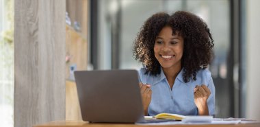 Heyecanlı mutlu Asyalı Afrikalı kadın dizüstü bilgisayara bakıyor, online galibiyeti kutluyor, neşeli genç Afrikalı kız sevinçten çığlık atıyor, bir ofis arka planında izole edilmiş.
