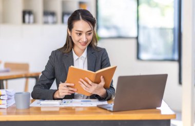 Neşeli Asyalı iş kadını çalışma alanı ofisinde çalışıyor. Ofisteki ahşap masada matematik finansmanı yapmak, vergi, muhasebe, finansal konsebe.